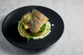 Stir-fried sea bass fillet with quinoa and broccoli garnish with creamy sauce, served in a black plate on a marble background. Royalty Free Stock Photo