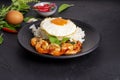 Stir-fried shrimp with basil Thai street food arranged on a black plate with a fried egg Thai spicy food Placed on a dark black