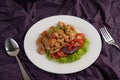 Stir shrimp macaroni on a white plate with fork, spoon, tomatoes and salad