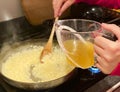Stirring in broth to a risotto rice in a frying pan on a home stove