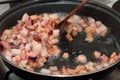 Stirring with a wooden spoon some frying bacon