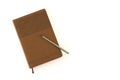 A stitched leather notebook with patterns on a brown cover and a gray pencil, isolated on a white table