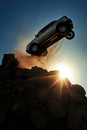 silhouette of a generic car crashing flying off a cliff. Stone cliff. dark blue and teal warm sky. Sun shining through the rocks.