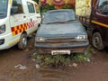 Stock photo of abandoned broken , damaged blue color car left in the scrap yard for recycling . White color ambulance and tempo