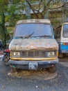 Stock photo of abandoned broken, damaged white color vans, motorcycle left in the scrap yard for recycling, green trees and