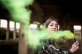 Brown hair girl holds a smoke bomb that throws yellow smoke around. Young girl wears an urban style, military jacket and piercing