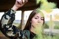 Brown hair girl holds a smoke bomb that throws yellow smoke around. Young girl wears an urban style, military jacket and piercing