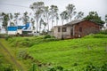 Stock photo of a house constructed with red bricks in between green grass and trees, blue color shelter, water tank and solar