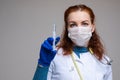 Stock photo portrait of a red-haired professional scientist in protection mask, white coat and glove holding a syringe