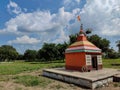 Stock photo small old hindu temple painted with orange color, situated in the middle of grass land, surrounded by green trees. Royalty Free Stock Photo
