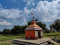 Stock photo small old hindu temple painted with orange color, situated in the middle of grass land, surrounded by green trees, Royalty Free Stock Photo