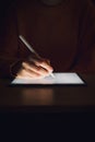 Stock photo of a woman`s hand writing on a tablet in the dark