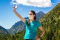 Stock photo of a young woman wearing a mask taking a selfie in the mountains and beautiful landscapes Royalty Free Stock Photo