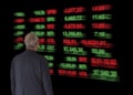 Stock trader man with glasses looking at stock prices on a light board.