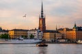 Stockholm old town at sunset with the church of Riddarholmen and a classic wooden boat passing by Royalty Free Stock Photo