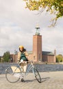 Beautiful smiling woman wearing old fashioned tweed dress holding a vintage bicycle in front of Stockholm City Hall Royalty Free Stock Photo