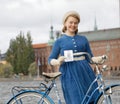 Closeup of beautiful smiling woman wearing old fashioned blue dress holding a retro bicycle in front of Stockholm City Hall Royalty Free Stock Photo