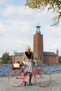 Laughing woman wearing old fashioned clothes holding a red vintage bicycle in front of Stockholm City Hall Royalty Free Stock Photo