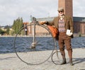 Senior man wearing old fashioned tweed suit holding a high wheeler bicycle in front of Stockholm City Hall