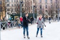 Young couple skating at a public ice skating rink outdoors in the city.