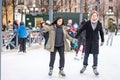 Young couple skating at a public ice skating rink outdoors in the city.