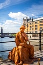 Male street performer on a bridge wearing makeup and gold colored clothing.