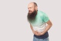 Stomach pain. Portrait of sick middle aged bald man with long beard in light green t-shirt standing, holding his painful belly and