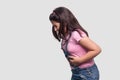 Stomach pain. Side view profile portrait of sick brunette young girl in pink t-shirt and blue overalls standing and holding her Royalty Free Stock Photo