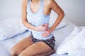 Stomach Pain. Unhealthy young woman with stomachache leaning on the bed at home Royalty Free Stock Photo