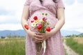 Stomach of the pregnant woman in a summer dress on the road outdoors, with flowers in hands. First pregnancy. On field Royalty Free Stock Photo