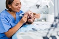 Stomatologist girl in uniform is taking visional inspection of a man in hospital