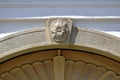 Stone arch above decorative wood gate. Ornamental carved keystone with flower motive. White stucco exterior wall elevation.