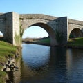 Stone arch bridge spans across a calm river, casting reflections on the water. Royalty Free Stock Photo