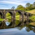 Stone arch bridge spans a tranquil river, with clear reflections in the water. The Royalty Free Stock Photo