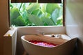 Stone bath tub with heart shaped flower petals near window with jungle view. Organic spa relaxation in luxury Bali bathroom Royalty Free Stock Photo