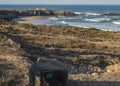 Stone with blue and green sign of Fishermans trail and view of Praia Grande de Almograve sand beach with ocean waves and