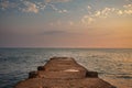 A stone breakwater stretching out to sea at orange sunset of the sun and the blue cloudy sky
