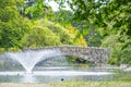 Stone bridge across pond with water fountain in park Royalty Free Stock Photo