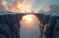 Stone bridge spans chasm between cliffs with people crossing. Dramatic sky with bright sun and clouds provides a backdrop. Royalty Free Stock Photo