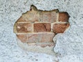 A hole in the wall. Chipped piece of plaster. Under the rough surface is a brick wall. The stone is broken and uneven.