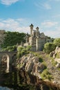 Stone castle with turrets stands on cliff with an arched bridge over water, surrounded by greenery under blue sky. 3d render Royalty Free Stock Photo