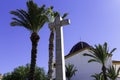 Stone cross and the dome of the church against the background of blue sky and palm trees. Symbol of faith, religion, Christianity