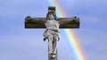 Stone cross with Jesus and blue sky with rainbow