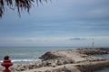 Stone dam with lighthouse and palm tree foreground. Pier on coast in the evening. Embankment on tropical seaside. Royalty Free Stock Photo