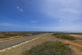 Stone desert of natural park on island of Aruba with asphalt road for vehicles against backdrop of Caribbean sea. Royalty Free Stock Photo