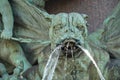 A stone devil on a fountain sculpture with water streaming from its mouth in two directions.