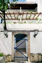 Stone fence with lattice gates near the house with a balcony, tree and greenery