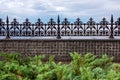 Stone fence made of square tiles and with iron forged peaks. Royalty Free Stock Photo