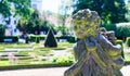 Stone figure of a baroque angel in front of a deliberately blurred background with a baroque garden