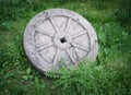 Stone granite wheel with rusted metal rim isolated on green grass. Royalty Free Stock Photo